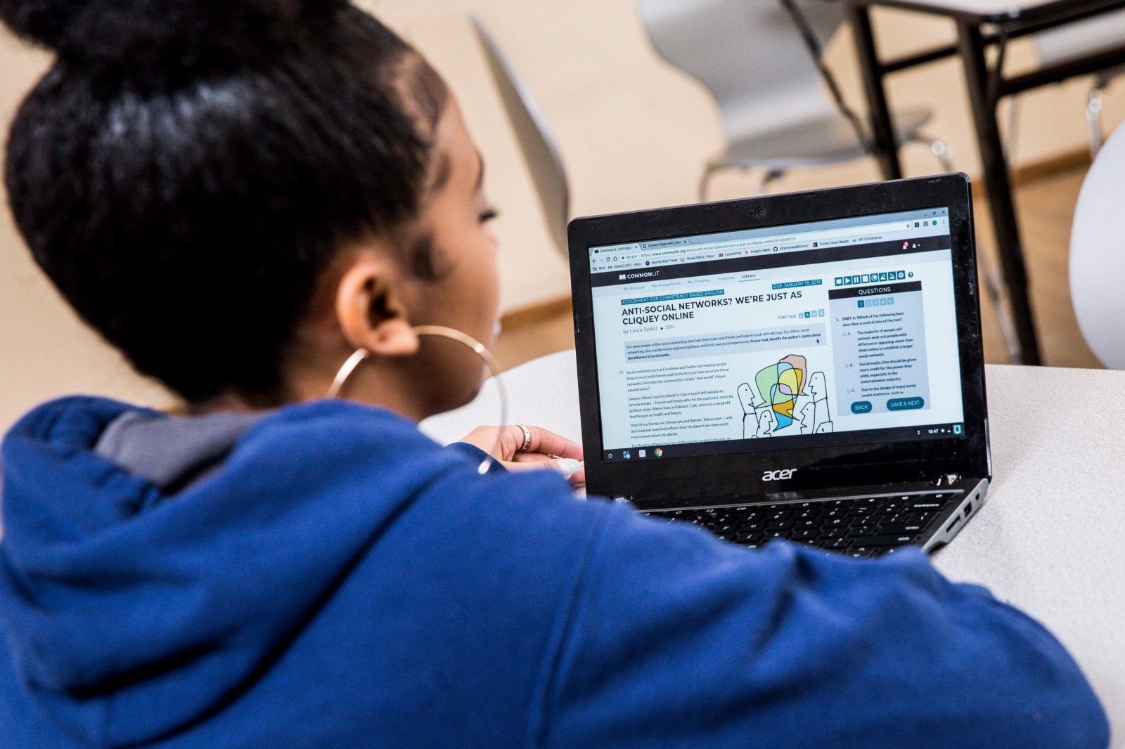 A student sitting at a table and looking at a CommonLit lesson on her computer. 