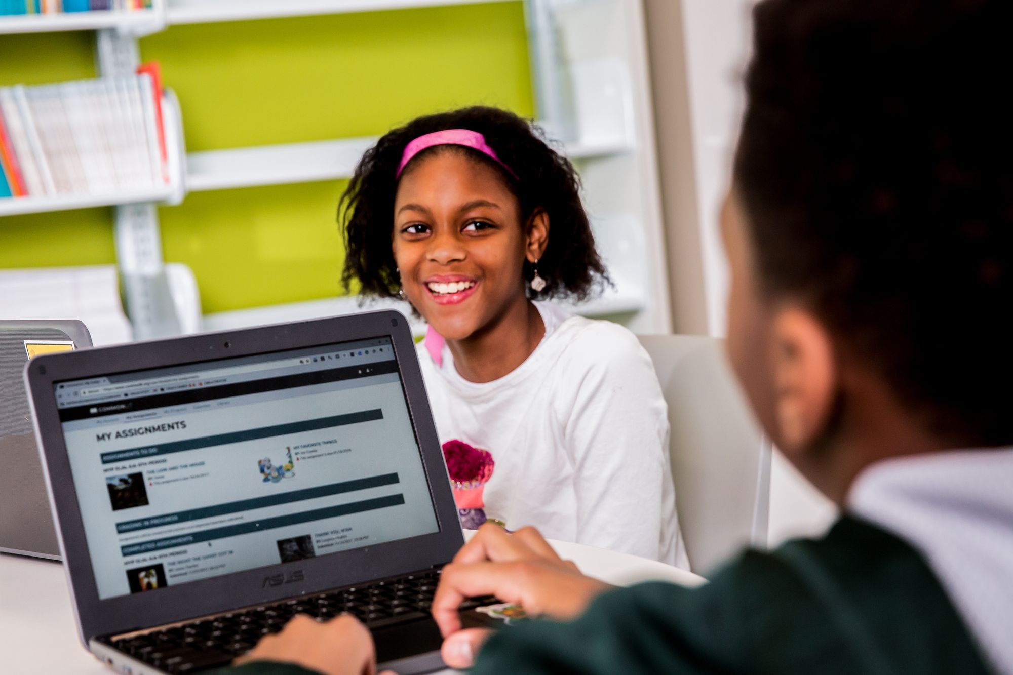 Girl smiles at classmate while working on CommonLit lesson. 