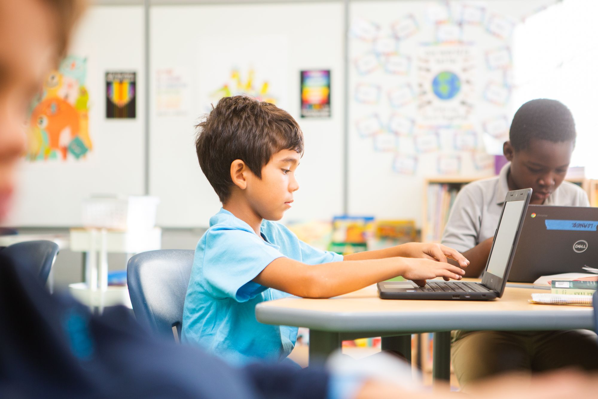 Niño trabajando en una computadora sentado en una mesa en su aula.