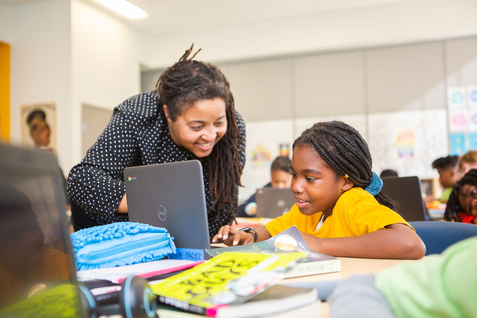 a teacher smiles as a student as she helps them with a lesson on their laptop