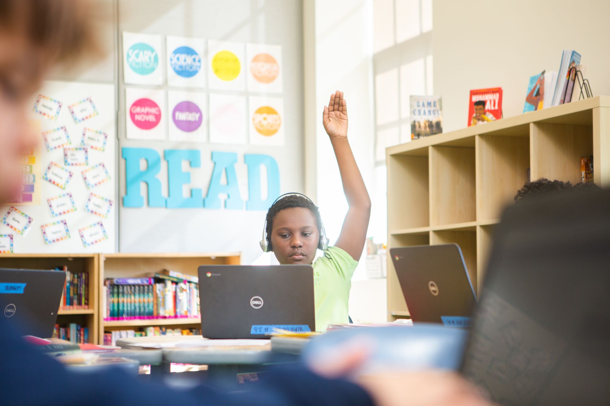 Student looking at a laptop screen with his hand raised.