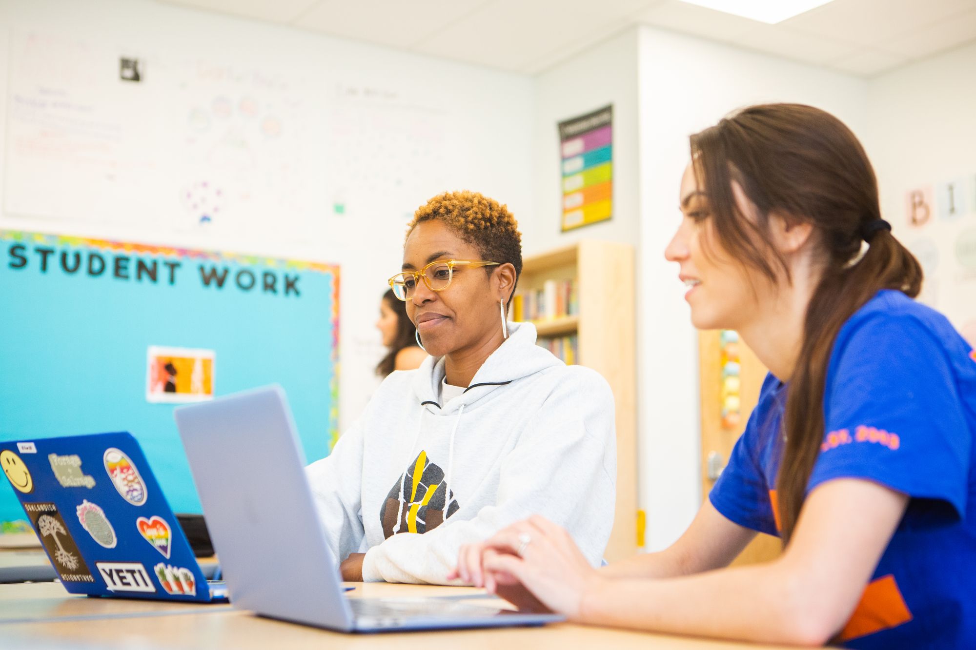 Two teachers work on laptops. 