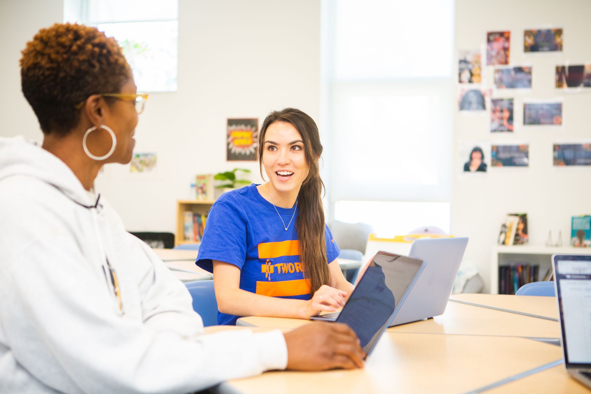 Two teachers conversing with their laptops open.