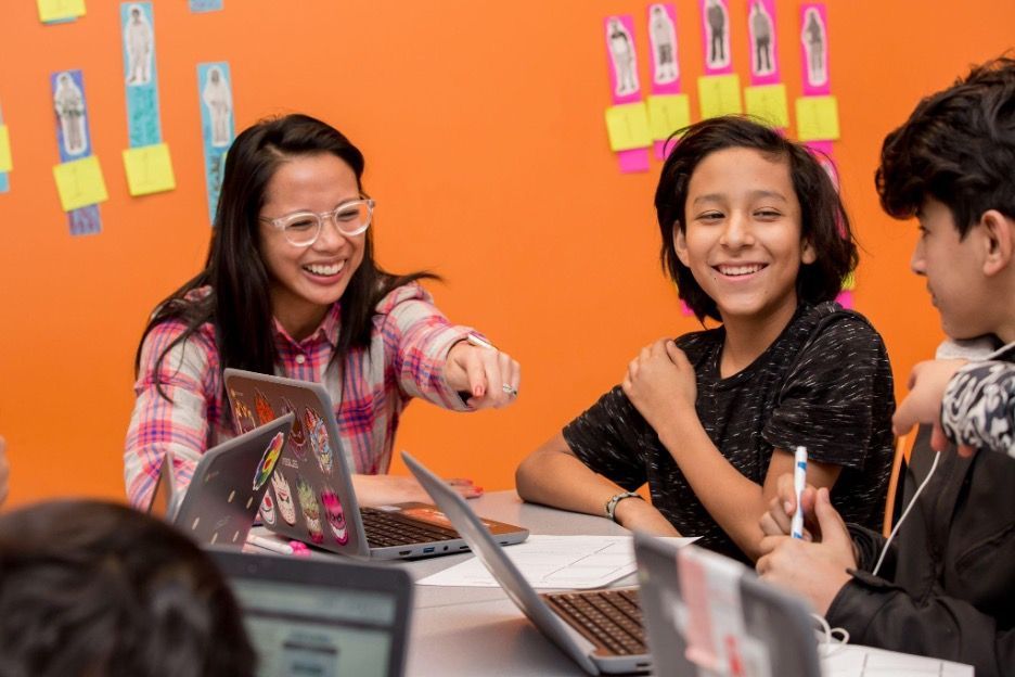 Docente trabajando con estudiantes en computadoras. 