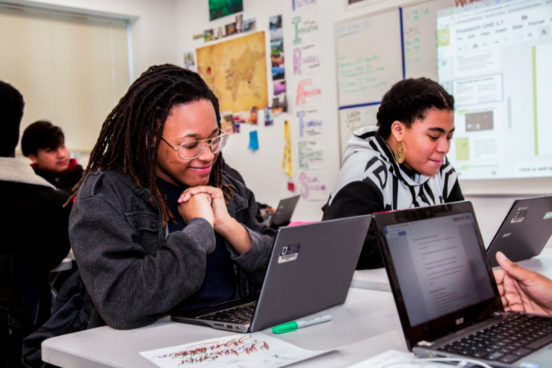 Two students sitting at a table and looking at their computer screens. 