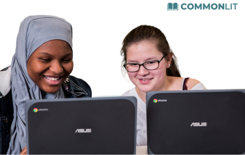 Two students sitting at a table and looking at their computers. 