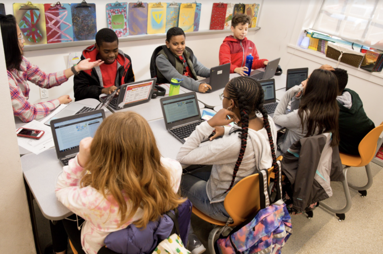 Students and teacher discuss lesson around table. 