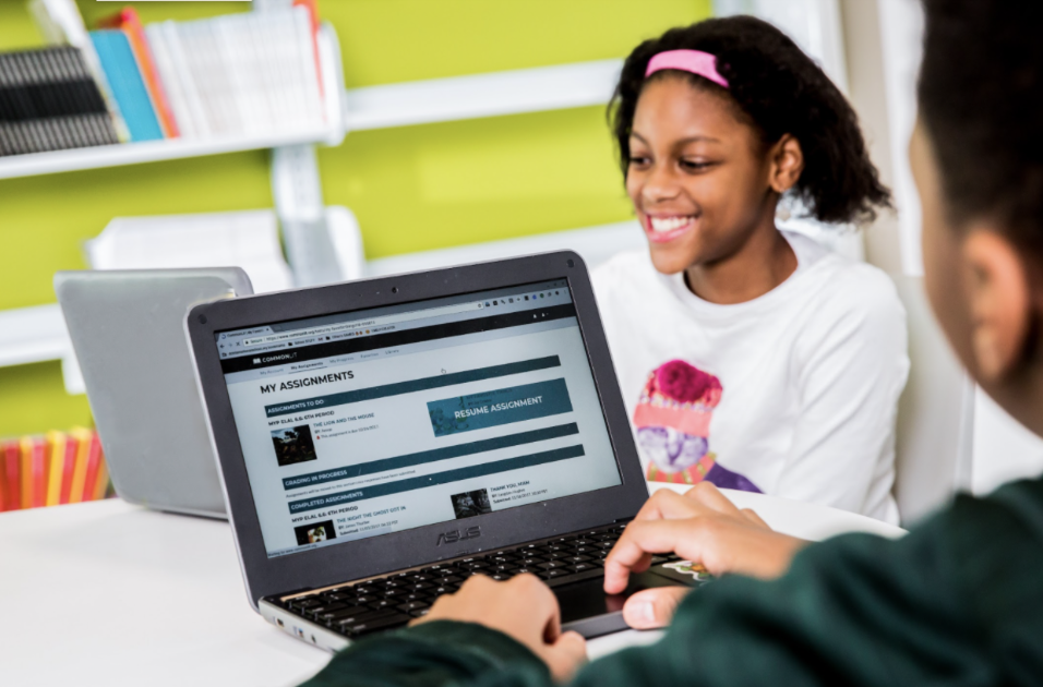 A girl smiles at her laptop while working on a CommonLit lesson.