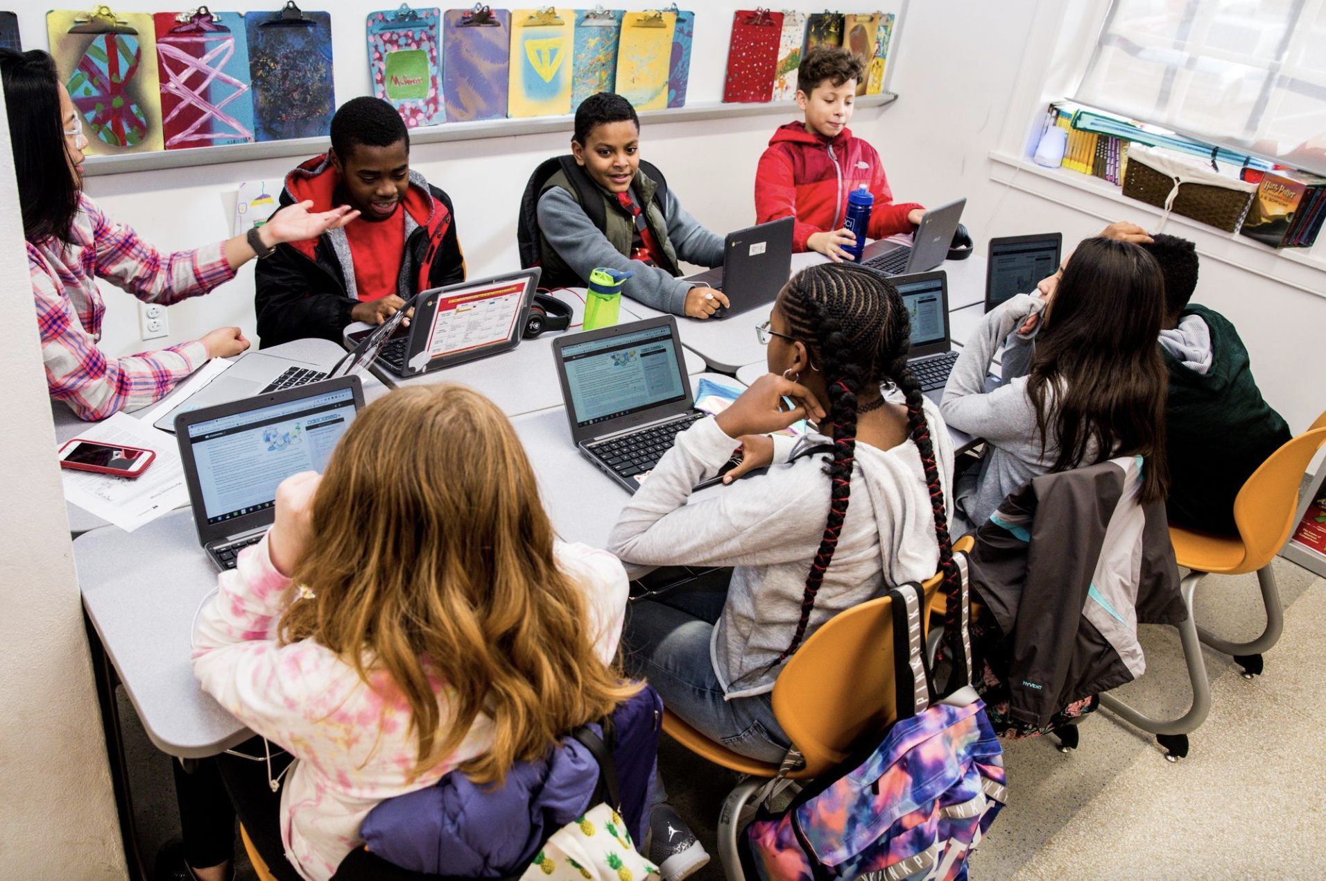 Middle school students and teacher discuss lesson around table. 